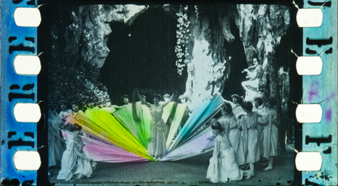 black-and-white film frames showing a woman and a semi-circle of dancers behind her. a semi-circle of ribbons spilling out from under the woman's feet are stencilled in different colours.